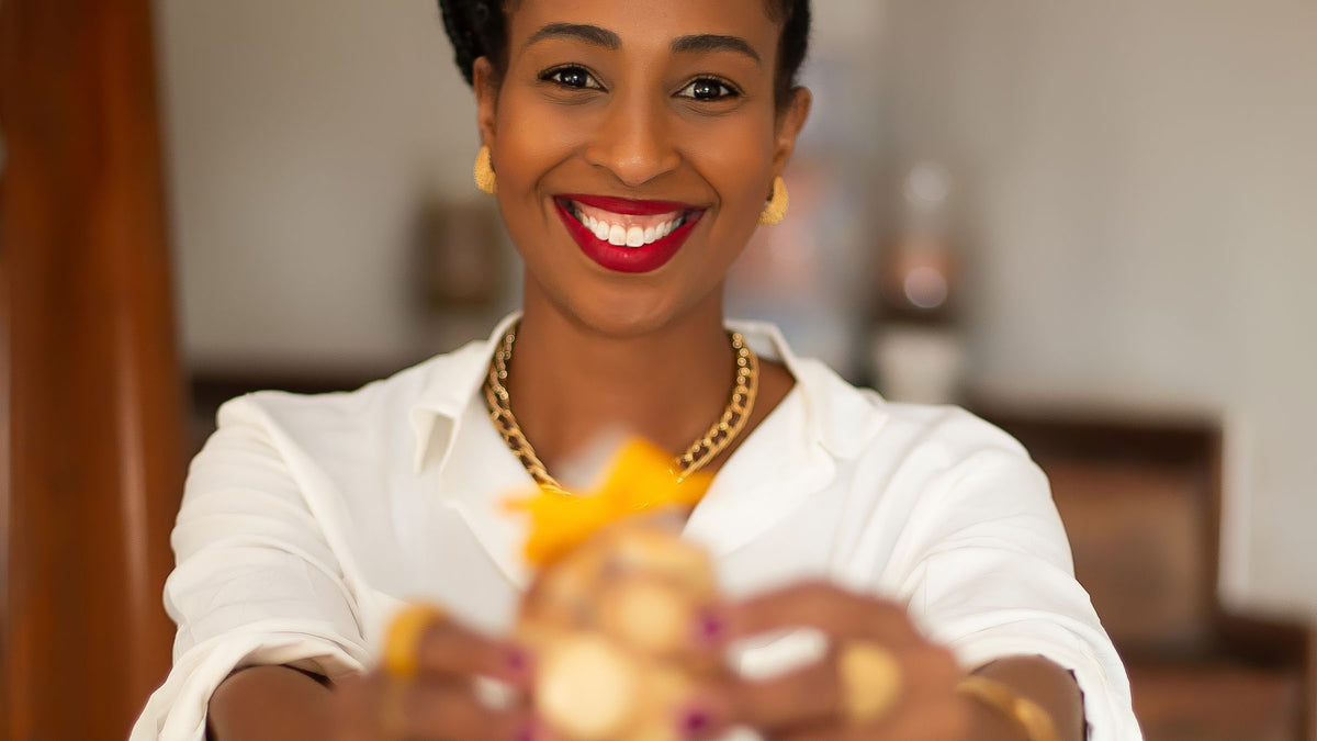 Carol Santos estendendo uma caixa de doces com laço amarelo, convite para apoiar a campanha da Maravilhas da Carol na Benfeitoria