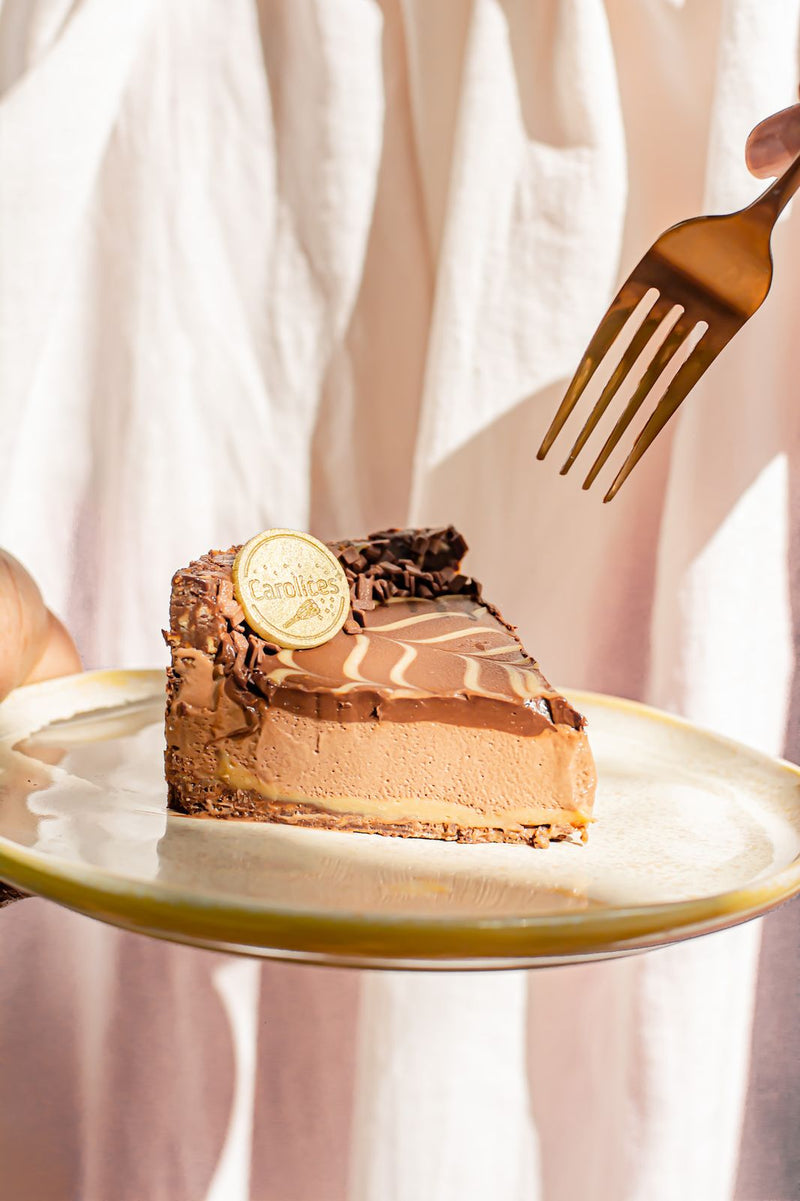 Fatia de torta de mousse de chocolate servida em prato dourado, segurada à mão
